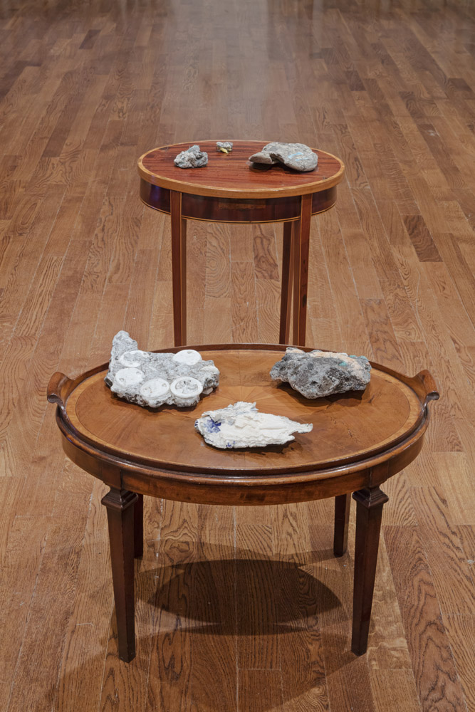 samples of greyish rocks with plastics of various plastics embeded inside them, sitting on two stately early twentieth century tables