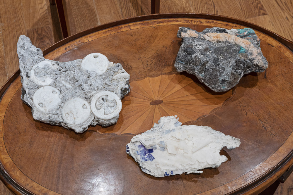 Greyish rockmatter fused with multi coloured plastics sitting on early 20th century side tables